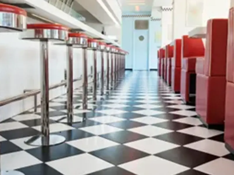 A diner 's checkered floor and red stools in the middle of the room.