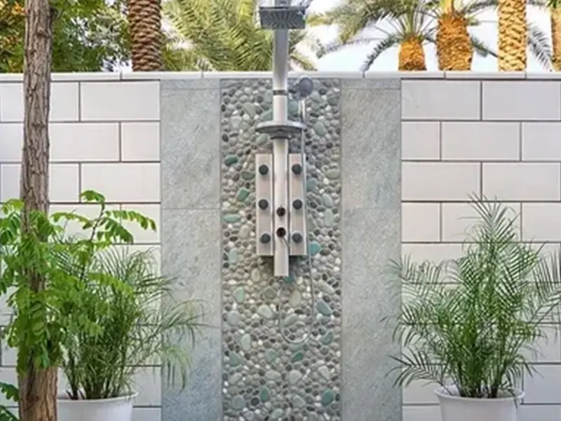 A stone wall with a shower head and plants