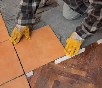 A person with yellow gloves on and holding onto tiles